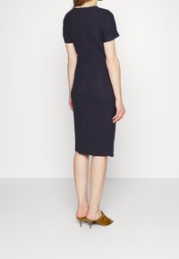 Marinblå figursydd klänning med korta ärmar, knälång, bakre dragkedja, slät textur. Bärs med gyllene klackskor.