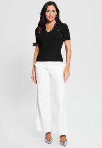 Polo top nero a righe con maniche corte, scollo a V e bottoni decorativi, abbinato a pantaloni bianchi a gamba larga e scarpe argento a punta.
