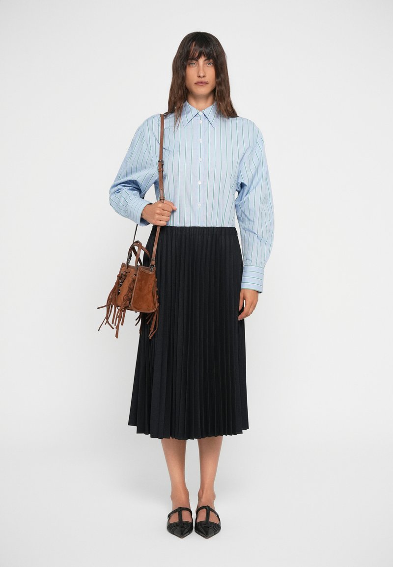 Blauw-wit gestreepte blouse met opgestoken mouwen, gecombineerd met een zwarte plooienrok. Gecombineerd met een bruine fringetassen.