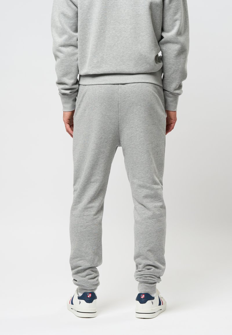 Grau Jogginghosen aus weichem Stoff, mit einem elastischen Bund und Bündchen am Knöchel. Sichtbare Nähte und eine lockere Passform. Weiße Sneakers mit Akzenten.