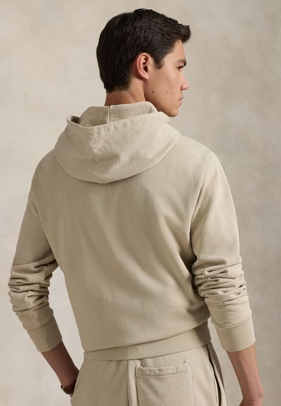 Beige hettegenser med avslappet passform, ribbede mansjetter og stor hette. Laget av strukturert stoff med subtile sømdetaljer.