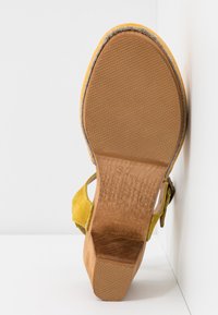 Semelle d'une sandale à talon en daim jaune avec talon bloc en bois face à l'appareil photo, montrant la taille 37 estampillée sur le bois.