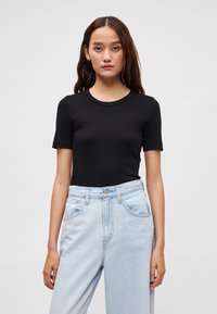 Černé krátké tričko s krátkým rukávem z měkké tkaniny, doplněné světle modrými džínami s vysokým pasem. Jednoduchý design bez potisků a log.