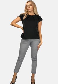 Czarna bluzka z krótkim rękawem z detalami w formie fałd, zestawiona z dopasowanymi spodniami w kratę. Wysokie obcasy dopełniają stylizację, podkreślając smukłą sylwetkę.