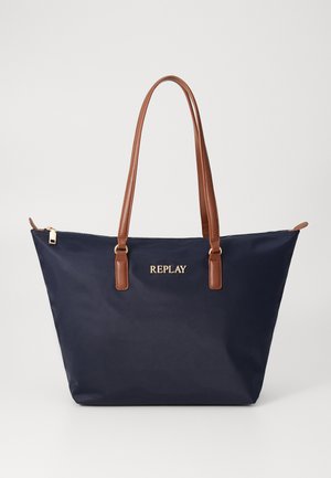 Navy blue tote bag made from nylon with brown faux leather handles and gold logo. Features a zip closure and a spacious, structured design.