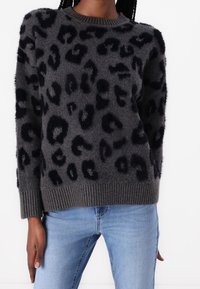 Maglione grigio con motivo leopardato nero, texture morbida, polsini e orlo a coste, scollatura rotonda. Indossato sopra jeans blu.