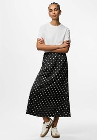 Mustru mustriga musta maksikleit satiinviimistlusega, elastse vöökoha ja küljetaskutega, mis on kokku pandud lihtsa valge T-särgi ja spordijalatsitega.