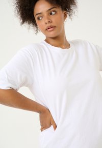 T-shirt en coton blanc à manches courtes et col rond. Le tissu semble doux, avec une coupe décontractée et une texture subtile.