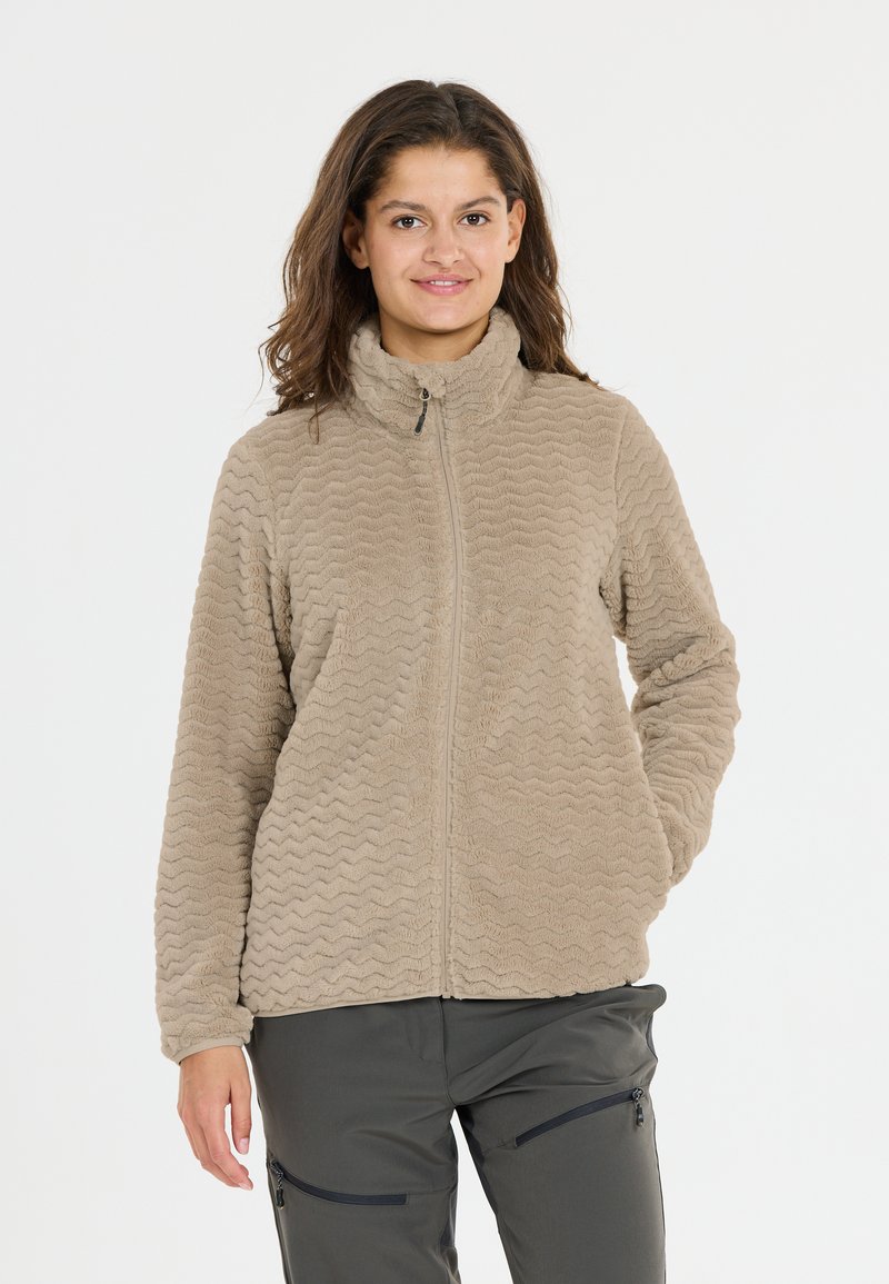 Beige fleece jack met golvende textuur, hoge kraag en een volledige ritssluiting. Draag het over donkergrijze broek met ritszakken.