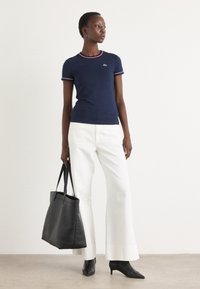 T-shirt marine avec accents rouges et blancs côtelés, associé à un pantalon blanc à jambes larges. Accessoirisé avec un sac en cuir noir et des escarpins noirs pointus.