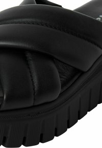 Sandalias deslizantes de cuero negro con suela gruesa y texturizada y un diseño de tira trenzada. Presentan una plantilla suave y acolchada para mayor comodidad.