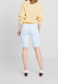 Bermudas de mezclilla azul claro con un corte ajustado, combinadas con un suéter amarillo de punto holgado y zapatos de tacón bloque blanco.