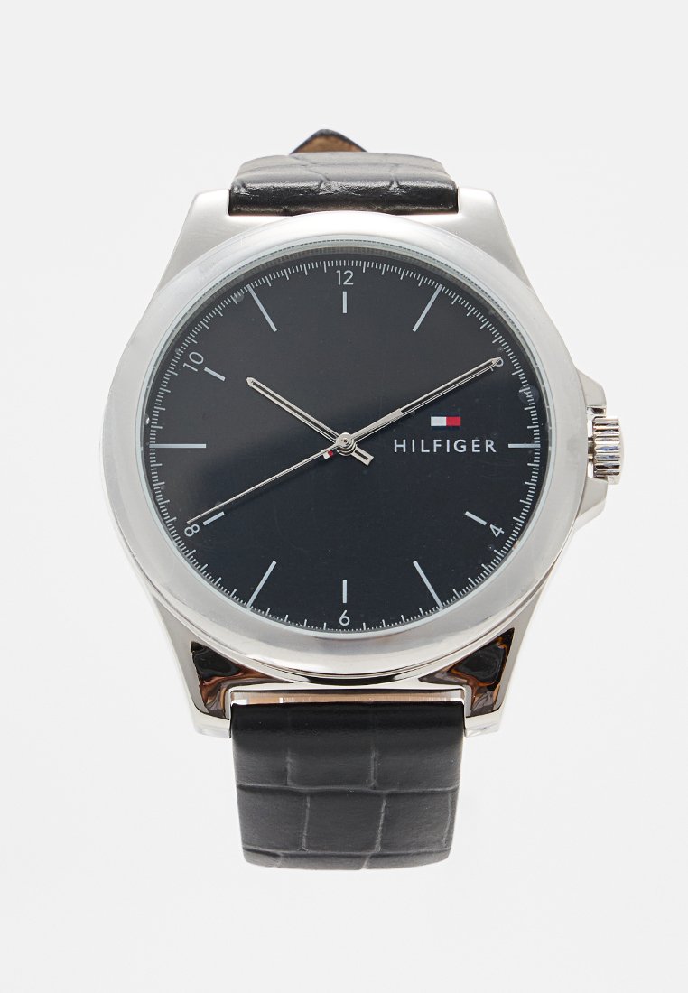 Zilveren roestvrijstalen horloge met zwarte wijzerplaat, zilveren uurmarkeringen en zwarte lederen band met krokodillenpatroon. Merkennaam: Hilfiger.