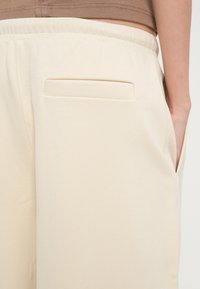 Pantaloni largi bej dintr-un material moale, cu un buzunar frontal plat și talie elastică pentru confort. Textură netedă, design minimalist.