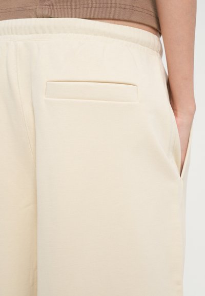 Beige laiad püksid pehmest kangast, millel on lame eesmine tasku ja elastne vöökoht mugavuse jaoks. Sile tekstuur, minimalistlik disain.