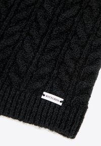 Czarna dzianinowa czapka z teksturowanym wzorem warkocza i prążkowanym brzegiem. Z białą metką z wytłoczonym napisem „WITTCHE”, dodającą szczegółów.