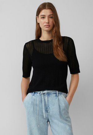 Schwarzes gestricktes Kurzarmoberteil mit Chevron-Muster, Rundhalsausschnitt und lässiger Passform, kombiniert mit hellblauen lockeren Jeans.