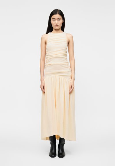 Robe longue sans manches en tissu pêche clair avec texture froncée au corsage, jupe fluide, et bottines noires.
