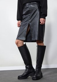 Black leather pencil skirt with front slit, paired with knee-high black boots featuring zippers and a chunky sole for added height.