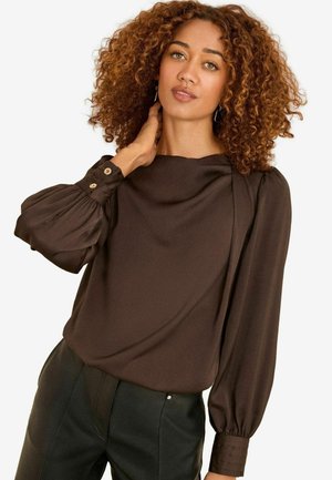 Dunkelbraune Bluse mit einem drapierten Ausschnitt, puffärmeligen langen Ärmeln und geknöpften Manschetten. Glatte Textur, kombiniert mit schwarzen Hosen.