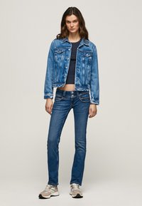 Jeansjakke i lys vask med kontrastsøm, klassisk krage, to brystlommer og cropped lengde, kombinert med blå jeans og sneakers.