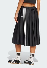 Back view of person wearing black pleated Adidas skirt with white stripes, white Adidas socks, and black Adidas sneakers.