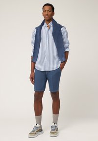 Blau gestreiftes Hemd mit Knöpfen, marinefarbener Weste und blauen Shorts. Beige und graue Sneakers mit blauen Akzenten. Lässiges Outfit mit einer entspannten Passform.