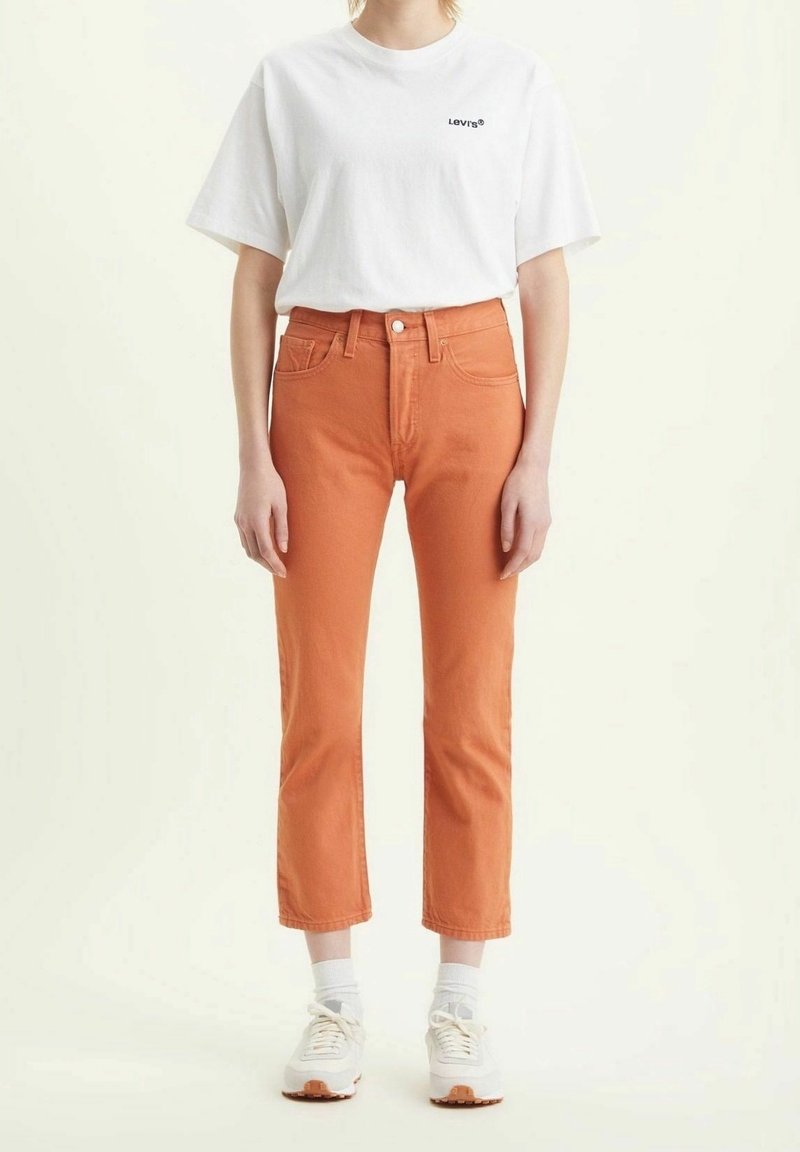 Jean en denim orange à taille haute et coupe droite, associé à un t-shirt blanc uni avec un logo noir, complété par des baskets blanches.