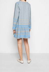 Niebieska sukienka w wzory z długimi rękawami, warstwowym dołem i teksturowanym wzorem. Materiał wydaje się lekki, z jasnoniebieskimi i beżowymi paskami.