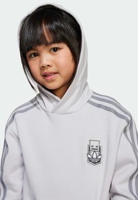 Vit hoodie med grå detaljer och ränder på ärmarna. Har en grafisk logotyp på bröstet. Mjuk känsla och avslappnad passform.