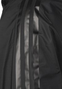 Czarna tkanina odzieżowa z pionowymi satynowymi paskami, o teksturowej powierzchni i niewielkim połysku. Projekt jest schludny i nowoczesny.