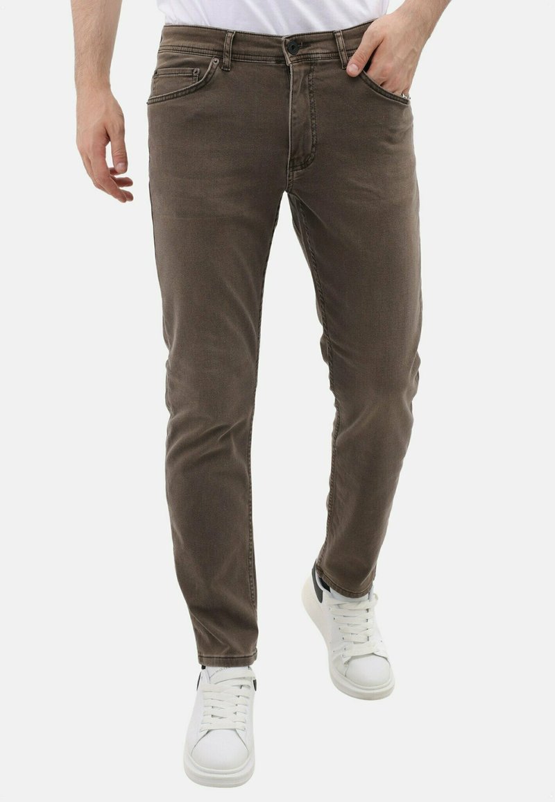 Bruine denim jeans met een slim fit, voorzien van voorzakken, een knoop- en ritssluiting, en subtiele vervaging. Gecombineerd met witte sneakers.