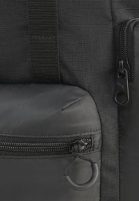 Zaino in tessuto nero con materiale testurizzato, scomparti con zip e dettaglio a forma di anello circolare sulla parte frontale. Design compatto per la portabilità.