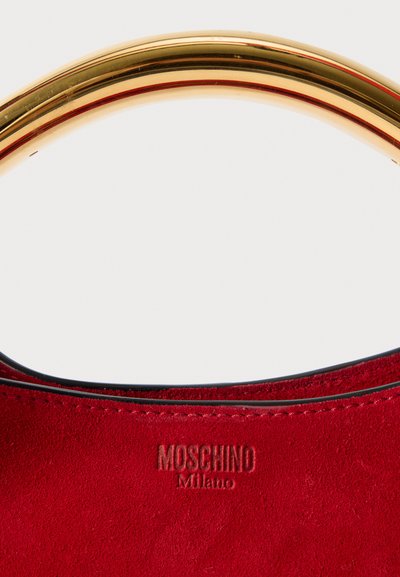 Crvena suđena torba s zlatnim metalnim ručkom. Sadrži urezani "Moschino Milano" logo s prednje strane. Glatka, mekana tekstura.