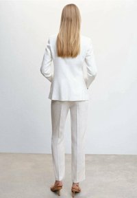 Blazer bianco in lino e pantaloni abbinati, design aderente, texture liscia, abbinati a sandali nudi con tacco alto. Visuale posteriore mostrata.