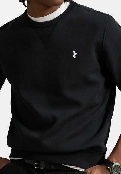 Sort sweatshirt lavet af bomuld, med rund udskæring, ribbede manchetter og et lille hvidt logo på brystet. Subtil tekstur, minimalistisk design.