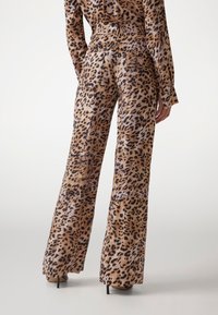 Pantalone širokog kroja od tkanine sa uzorkom tigra, glatke teksture, s više stražnjih džepova i visokim strukom. Tkanina sadrži tople nijanse smeđe i crne boje.