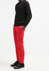 Czarny sweter o fakturowanej powierzchni z długimi rękawami, czerwone spodnie slim fit oraz czarne trampki z błyszczącymi akcentami. Prosty design, bez dodatkowych detali.