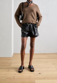 Hnědý pletený svetr, volný střih, s výstřihem do V; černé šortky z umělé kůže, skládací design, pásek; černé sandály na podpatku, otevřená špička, blokový podpatek.