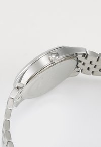 Montre en acier inoxydable argenté avec un boîtier lisse et poli, une couronne ronde marquée "BOSS" et un bracelet à maillons texturé.
