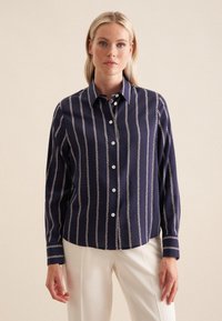 Camicia blu navy con bottoni, motivo a catena verticale, maniche lunghe e colletto. Realizzata in un tessuto liscio con una leggera brillantezza complessiva.