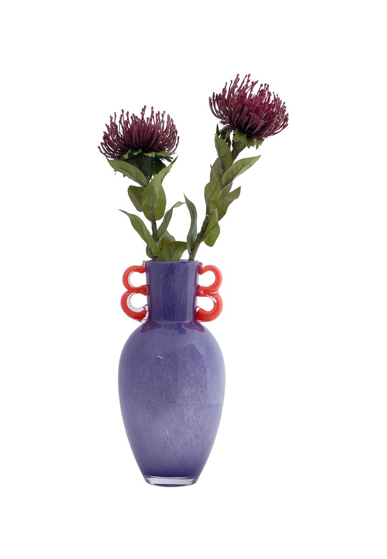 Jarrón de cerámica morado con un acabado brillante, que presenta dos asas decorativas rojas y sostiene flores artificiales de color púrpura oscuro con hojas verdes.