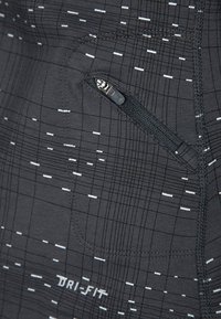 Tissu Dri-FIT noir avec un motif en grille, présentant des lignes blanches et un petit détail de poche zippée pour un rangement sécurisé.