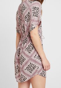 Woman wearing a short-sleeve, pink patterned dress with black and white leopard print, tied at the waist, shown from the back and side.