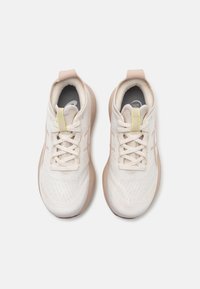 Zapatillas deportivas ligeras en malla color blanco roto con un patrón texturizado, acentos en rosa y suelas de goma beige. Incluyen cordones y un collar acolchado.