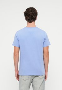 T-shirt de manga curta azul claro, feito de algodão, com decote redondo e uma textura suave. Corte reto, design minimalista, sem padrões.