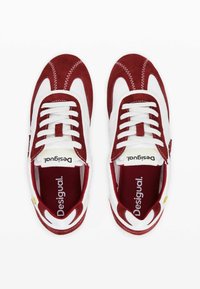 Adidași atletici roșii și albi, confecționați din suede și plasă, cu un vârf rotund, șireturi albe și un logo pe limba și pe talpa interioară.