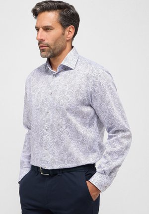 Witte blouse met lange mouwen en een ingewikkeld blauw paisleypatroon, met een kraag en knopen. Gecombineerd met donkerblauwe broek.