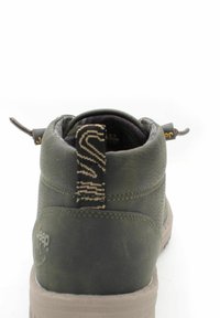 Stivale alla caviglia verde in pelle con finitura testurizzata, collare imbottito e un'etichetta di estrazione decorata. Presenta una suola beige e una marcatura visibile.