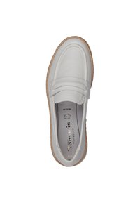 Mocassin en cuir blanc avec une semelle en tan texturée, présentant un design couturé et une sangle sur le dessus. L'intérieur montre les détails de la marque.